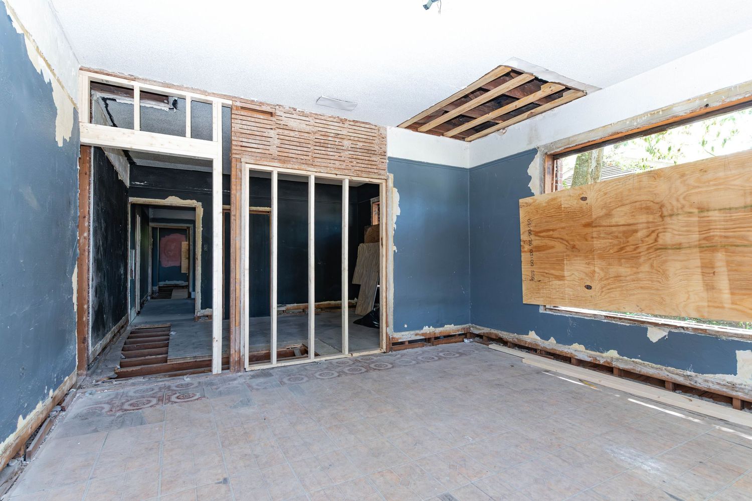 Interior of a home mid-renovation with exposed wood framing, blue walls, and boarded windows during remodeling.