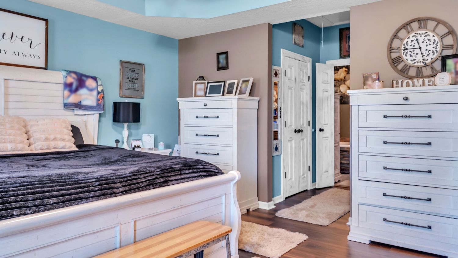 Cozy bedroom with white furniture, blue accent walls, dark hardwood floors, and a walk-in closet with elegant home decor.