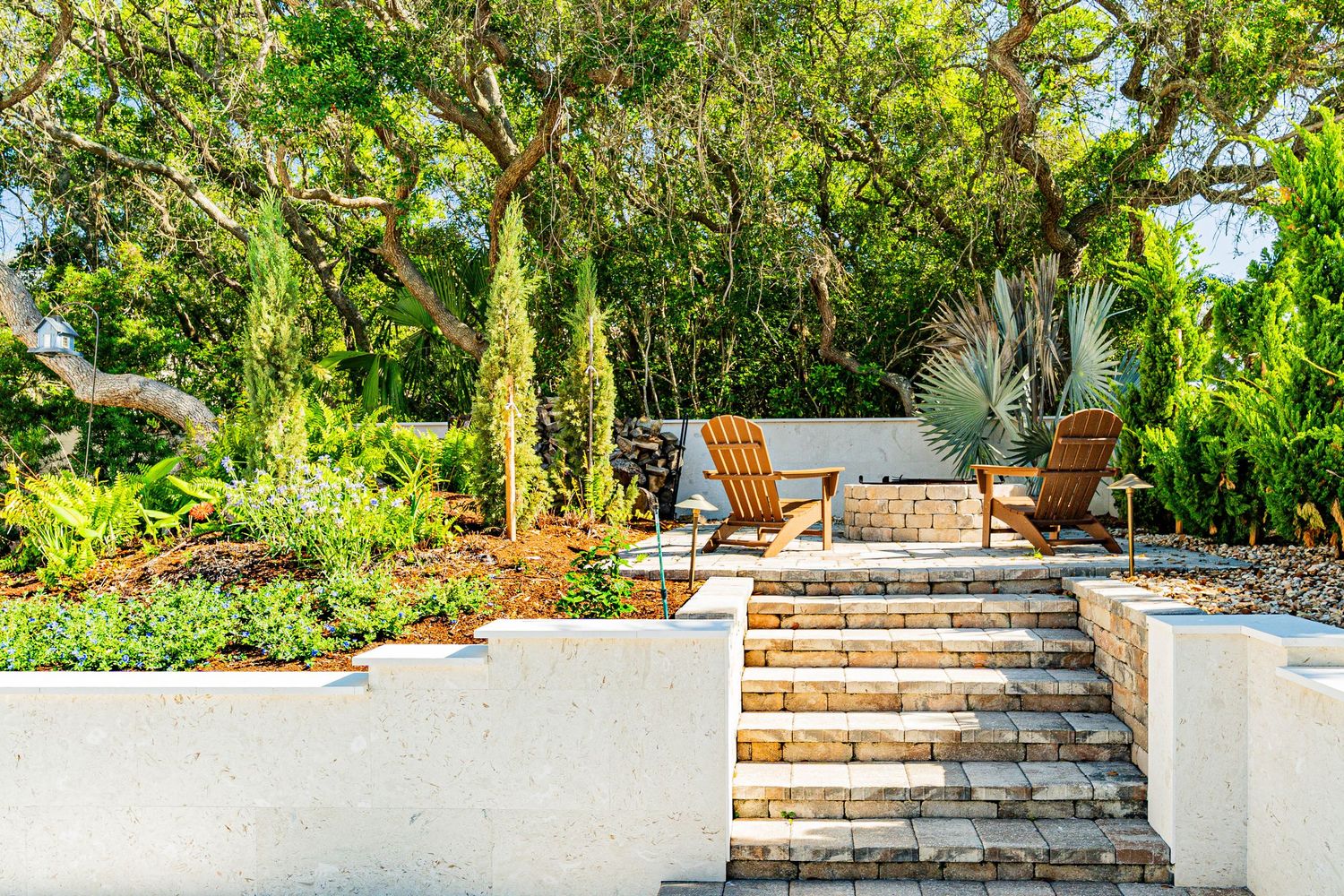 Terraced garden with stone steps, wooden chairs, lush greenery, and Mediterranean plants in a sunny outdoor patio in Fernandina, Florida.