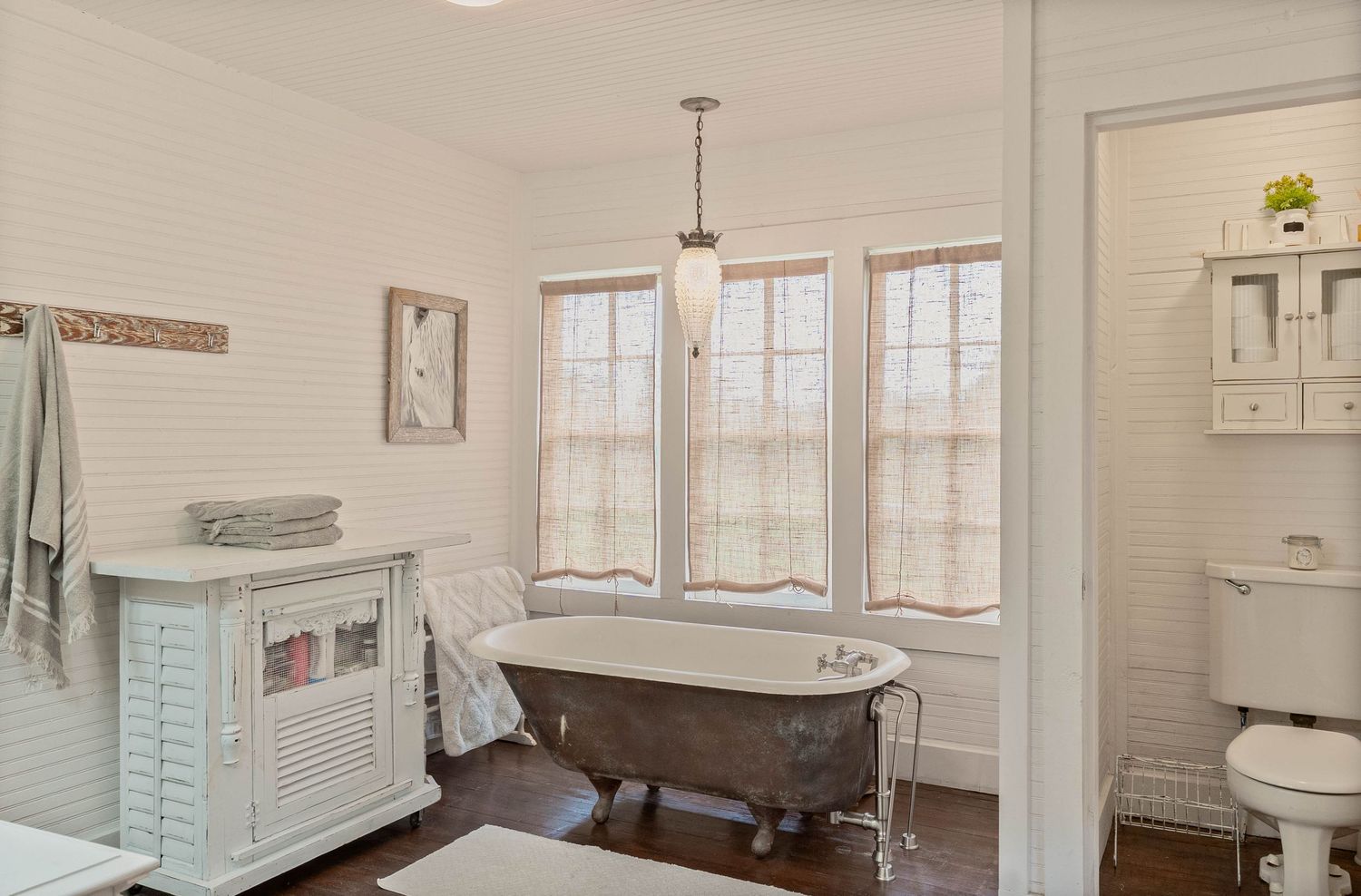 Elegant bathroom with clawfoot tub, pendant light, white shiplap walls, dark hardwood floors, and vintage vanity.