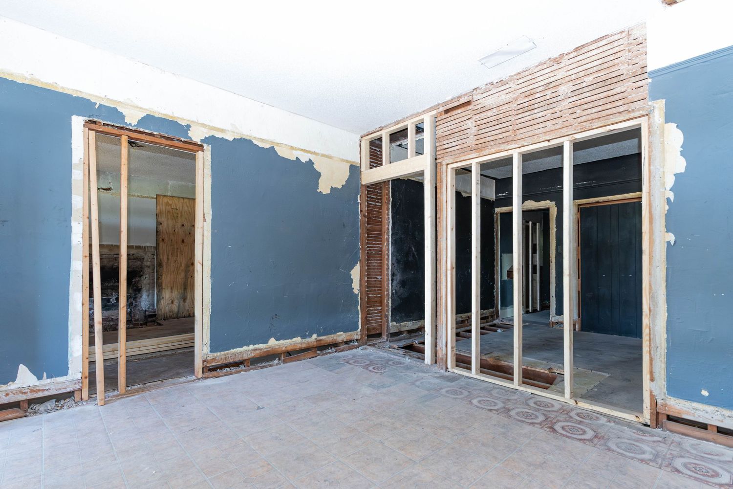 Interior room under renovation with blue drywall, exposed wood framing, and doorways in an empty space.
