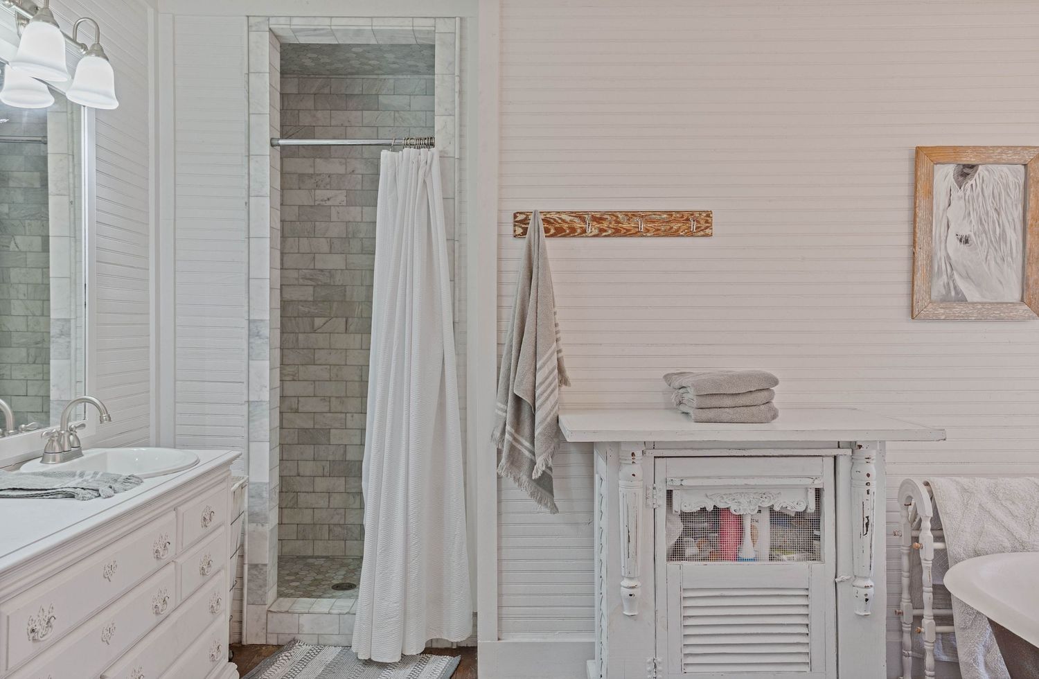 Bright white bathroom with walk-in tile shower, vintage cabinet, and shiplap walls featuring towel hooks and mirror.