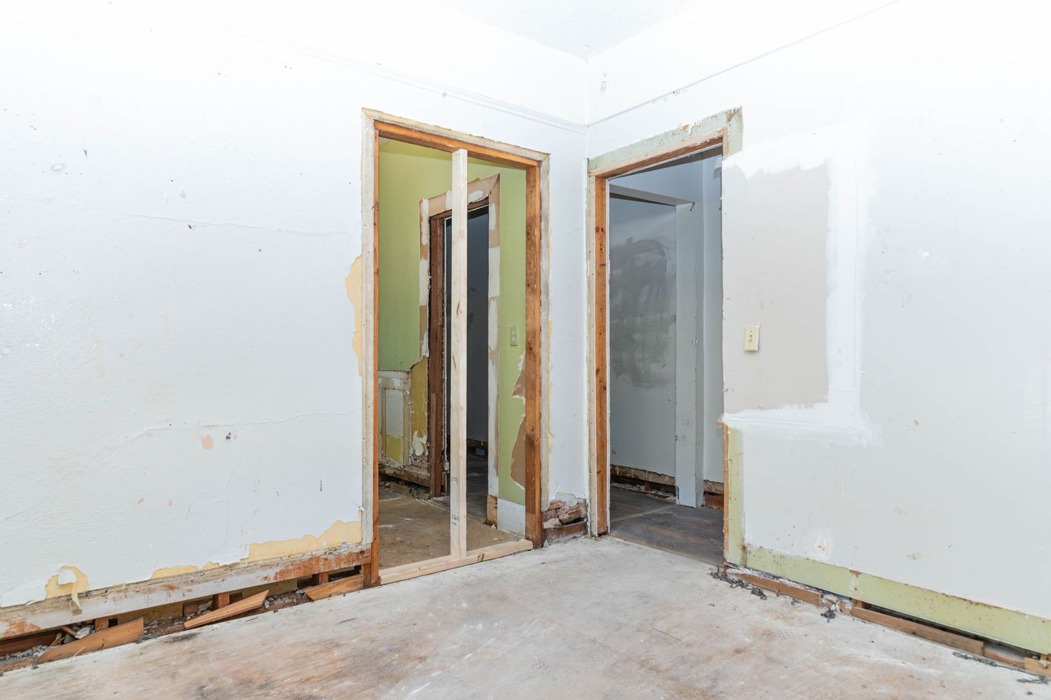 Unfinished room under renovation with drywall walls, two open doorways, and bare concrete floors.