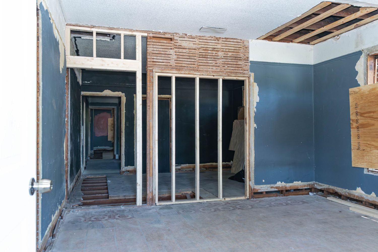 Interior room under renovation with exposed wall framing, blue walls, and debris on concrete floor.