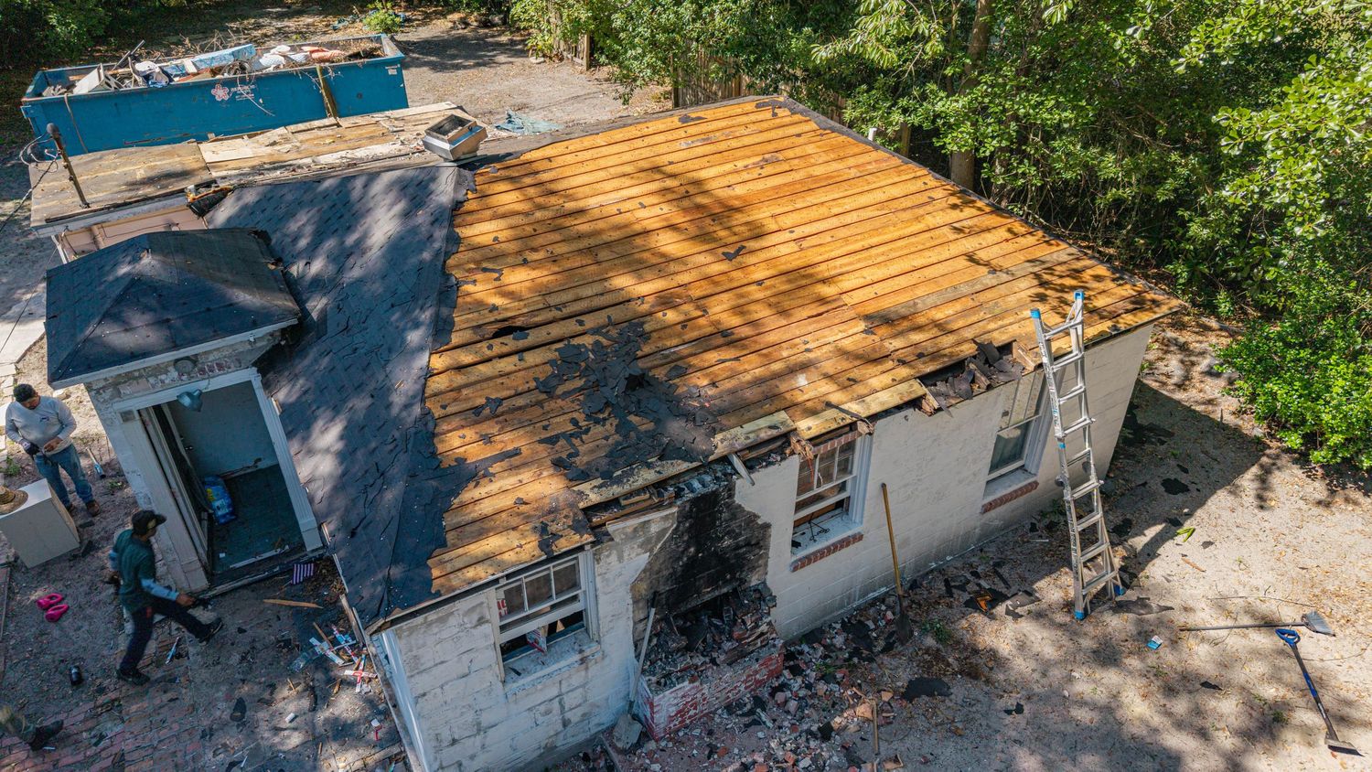 Aerial view of a house undergoing roof renovation with exposed wooden beams and a worker on site.