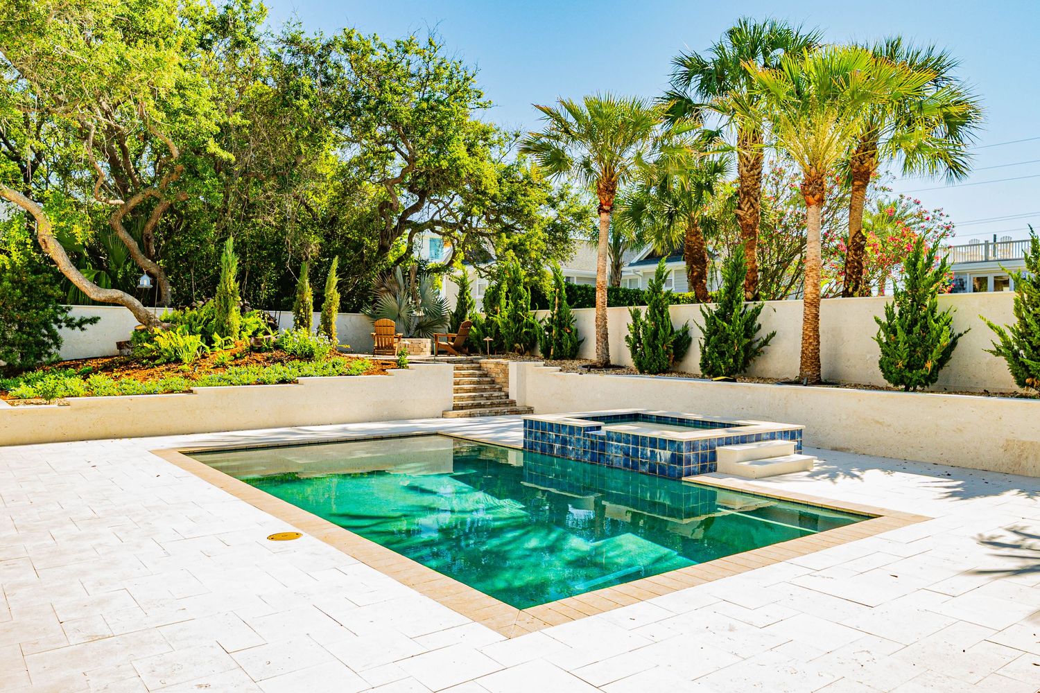 Luxury outdoor pool and spa surrounded by palm trees and white stone walls in a tropical backyard setting.