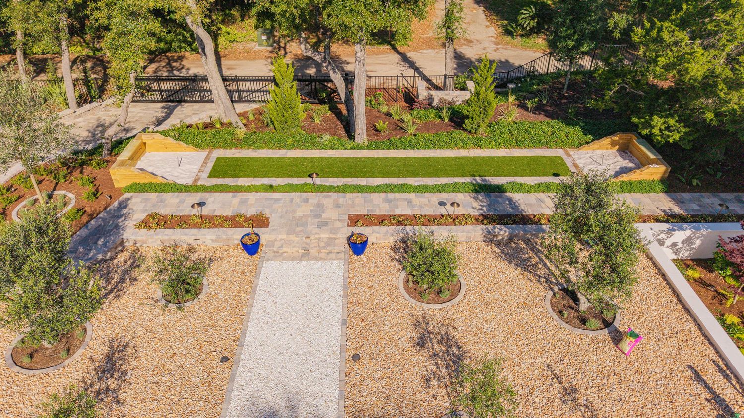 Aerial view of a symmetrical garden with gravel paths, green lawn, ornamental trees, and blue accent pots.