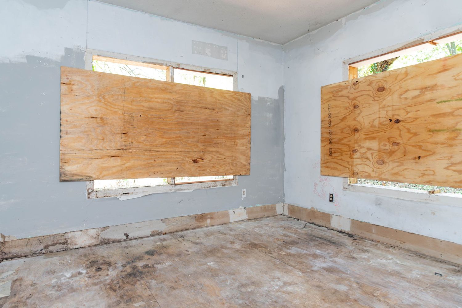 Abandoned room with boarded-up windows, peeling walls, and damaged flooring undergoing renovation.
