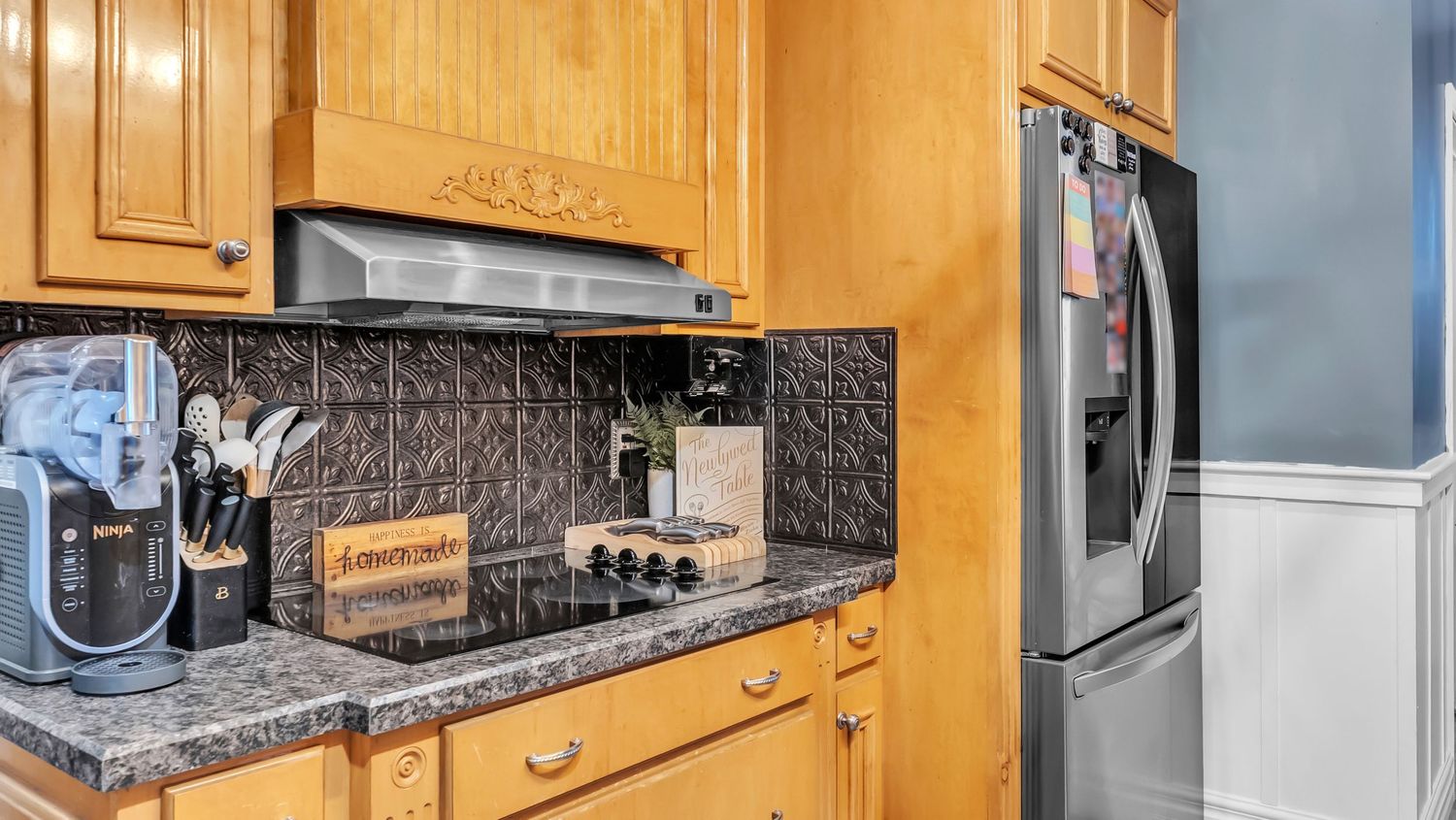 Oak kitchen cabinets with dark granite countertops, embossed tin backsplash, and stainless steel refrigerator.