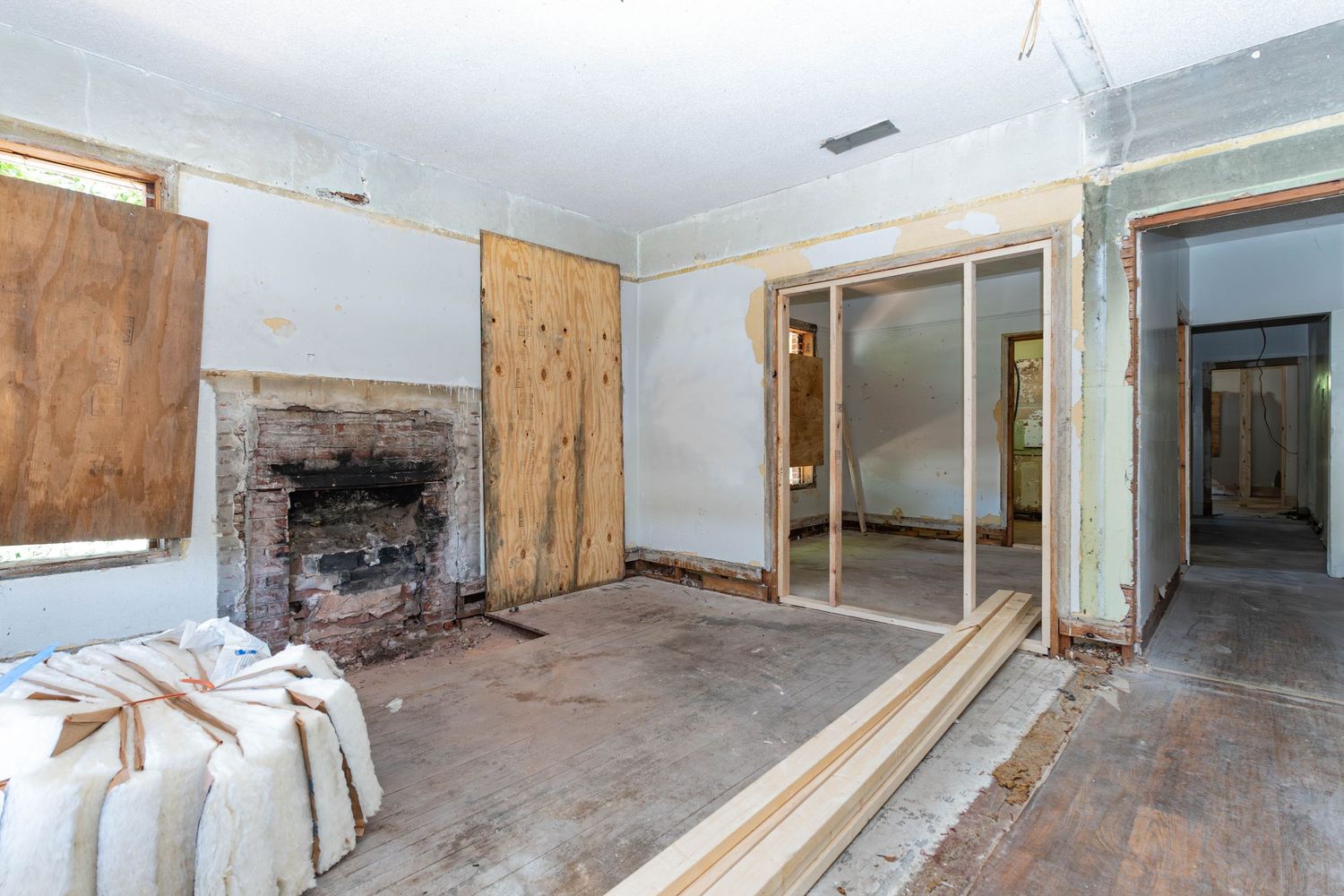 Abandoned room under renovation with fireplace, boarded windows, exposed walls, and sliding glass doors leading to hallway.