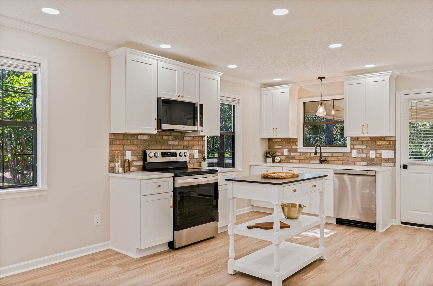 Modern white kitchen with stainless steel appliances, subway tile backsplash, hardwood floors, and a freestanding island.
