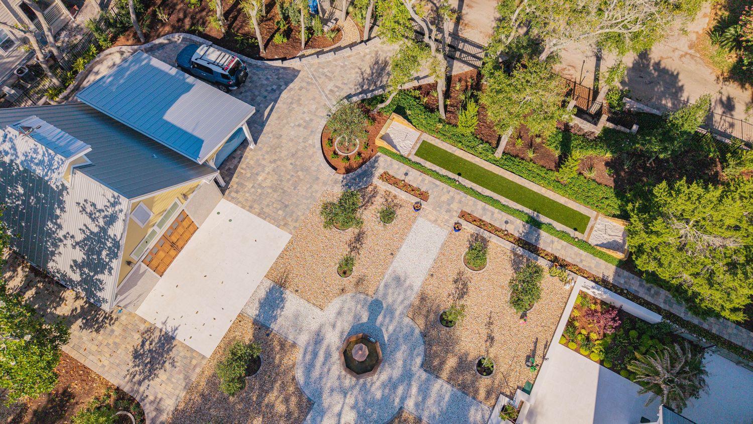 Aerial view of a modern home with lush landscaping, paved driveway, manicured lawn, and mature trees surrounding the property.