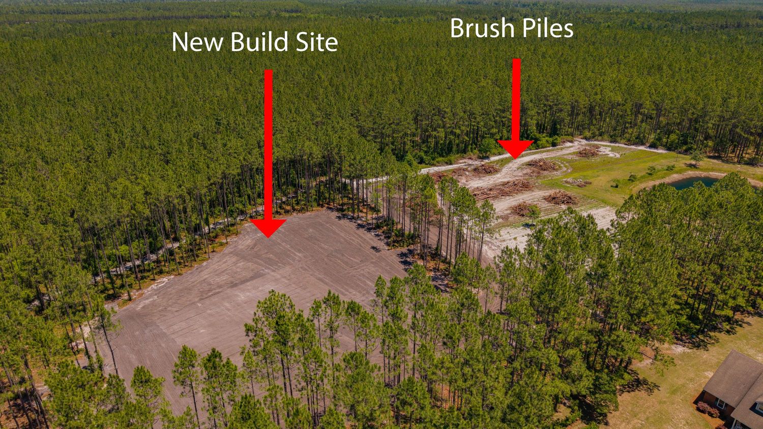 Aerial view of a forested property showing a new build site and brush piles marked with red arrows in a cleared area.