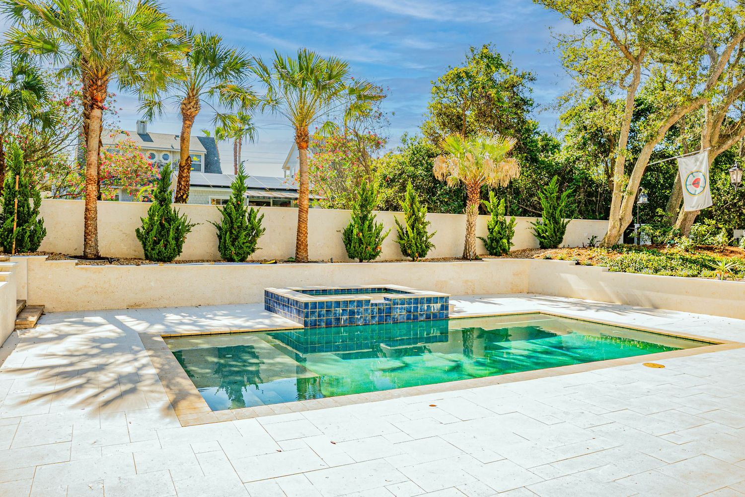 Luxury outdoor pool with spa, blue tile accents, white pavers, and lush palm trees in a private backyard.