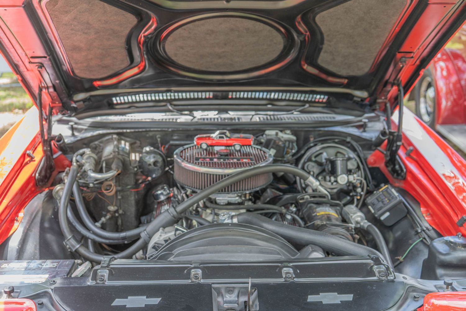 Red classic car engine bay showcasing a Chevrolet V8 motor with chrome air filter and detailed components.