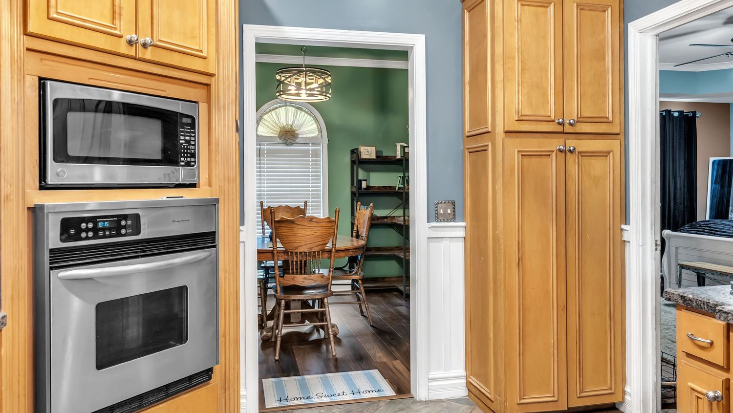 Modern kitchen with stainless steel wall oven, microwave, wood cabinets, opening to dining room with green walls.