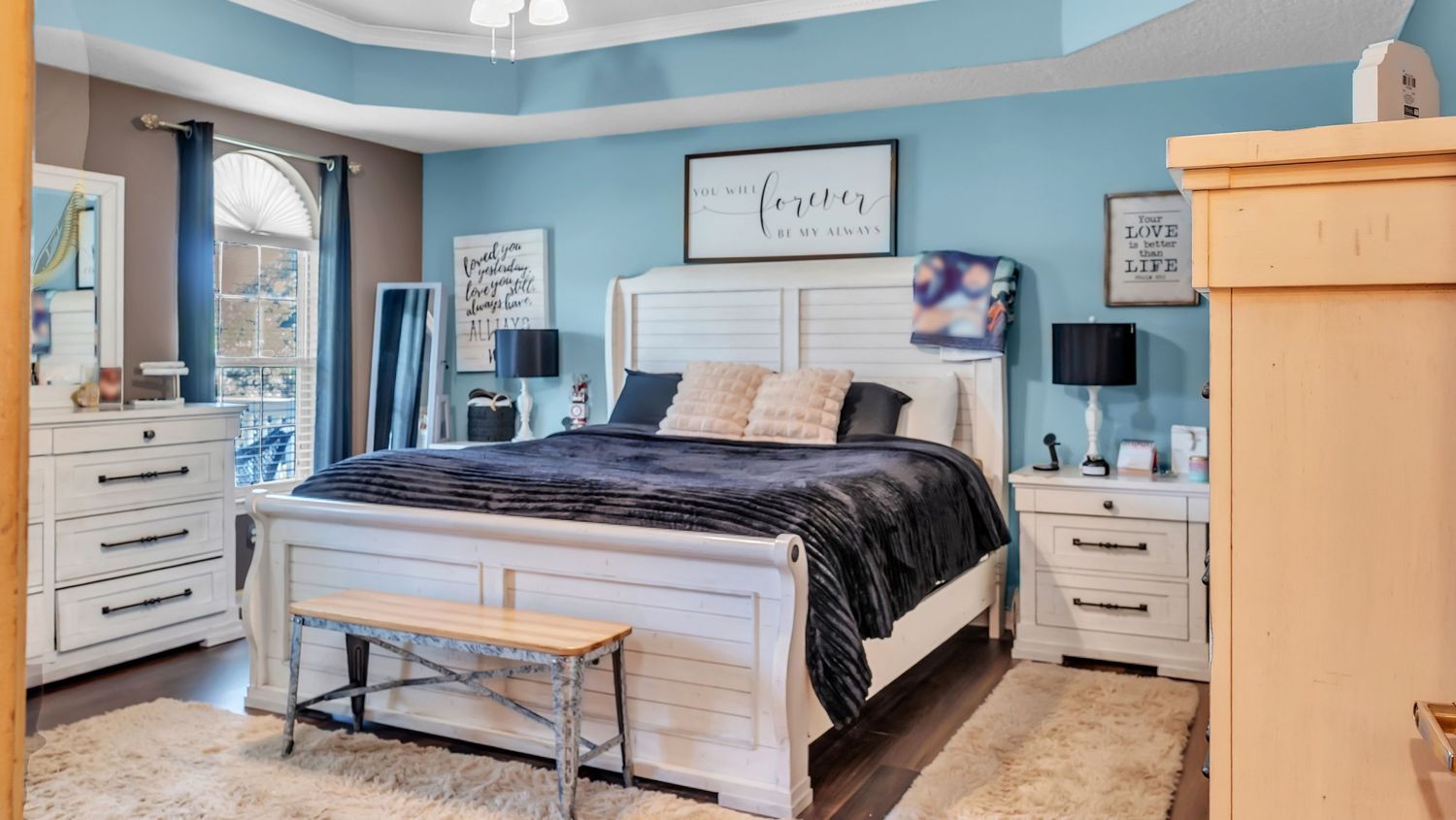 Elegant master bedroom with blue accent walls, white wood furniture, king bed with dark bedding, and hardwood floors.
