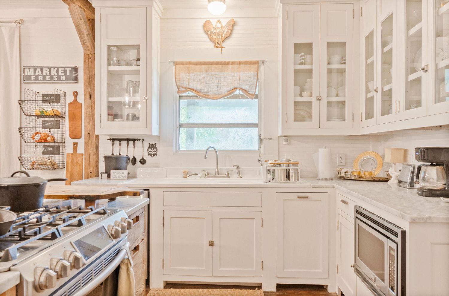 Bright white farmhouse kitchen with glass-front cabinets, apron sink, marble countertops, and a professional gas range.