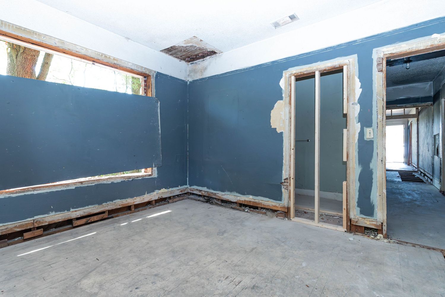 Empty room under renovation with blue walls, exposed framing around doorway, and concrete floors.
