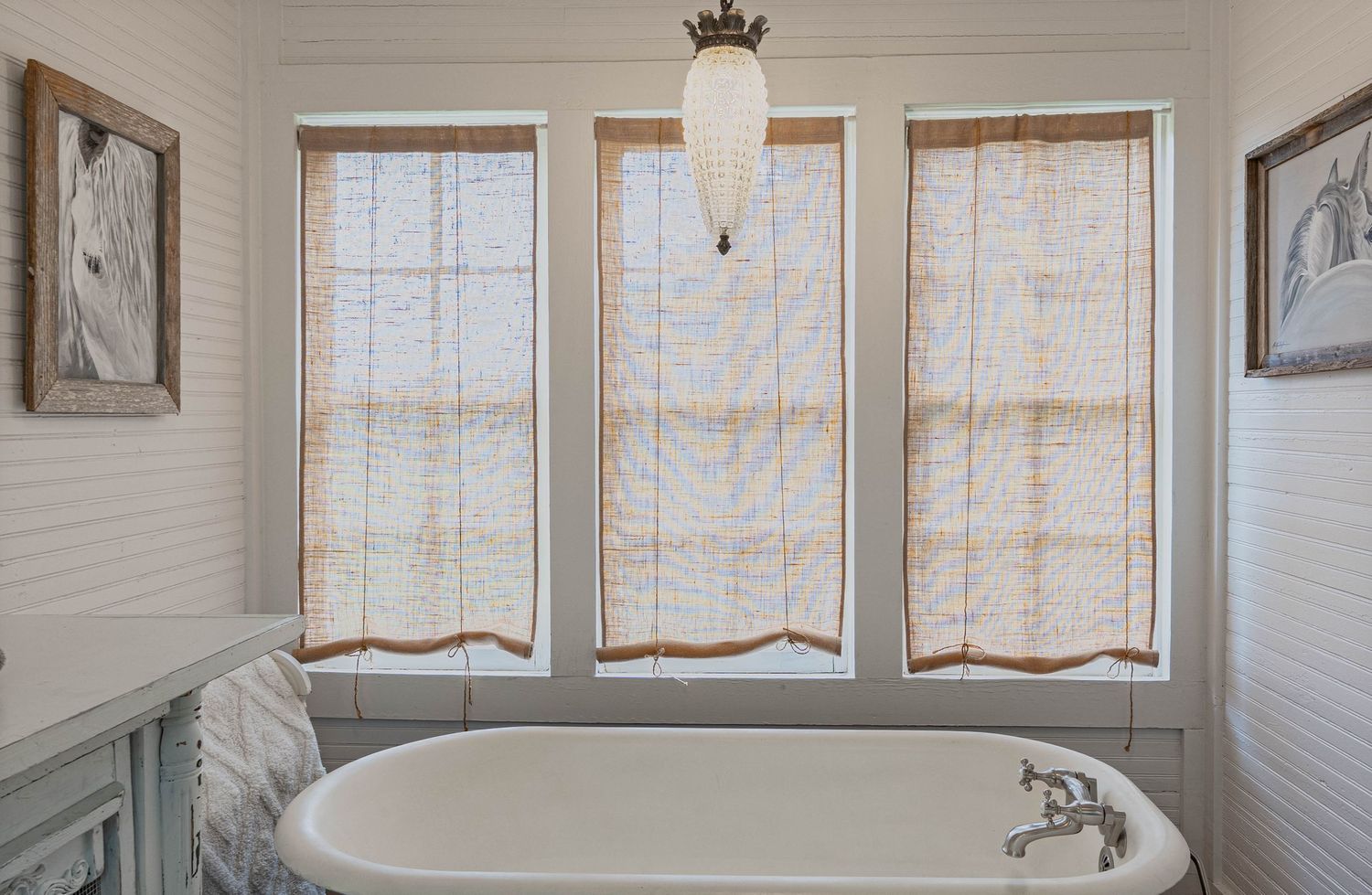 Vintage clawfoot bathtub beneath three bamboo roman shade windows in a bright white bathroom.