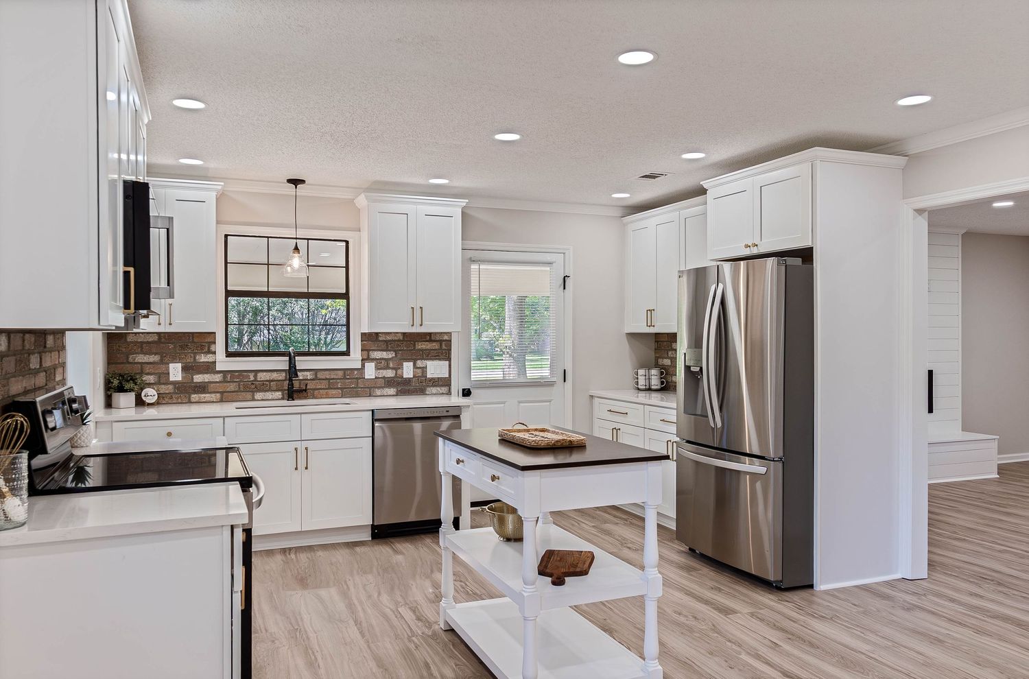 Modern white kitchen with stainless steel fridge, subway tile backsplash, island, and hardwood floors.