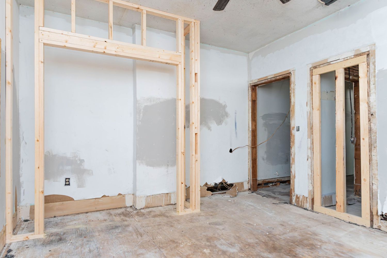 Interior room under renovation with wooden framing, drywall patches, and exposed concrete floors.