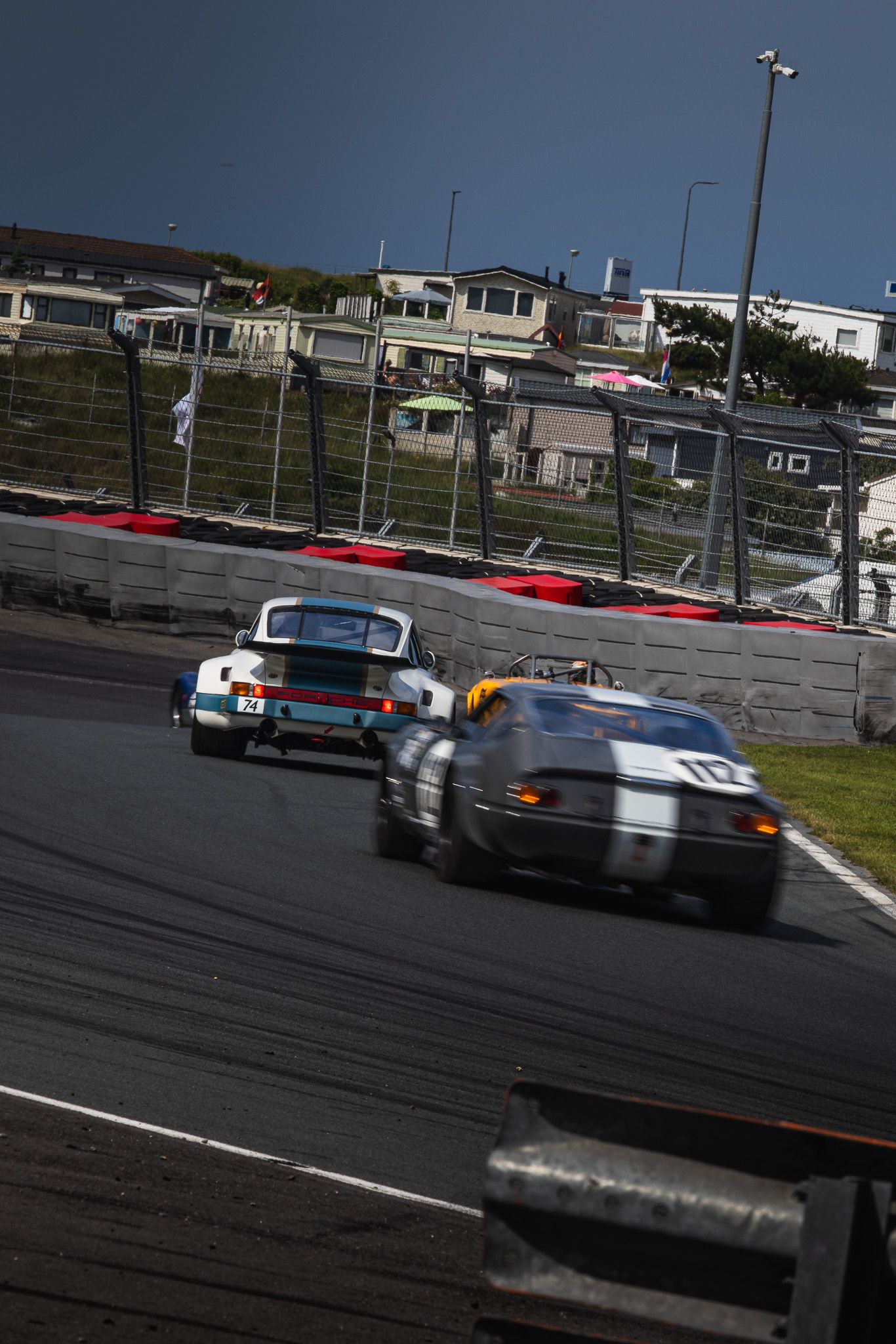 Vintage Porsche and classic sports cars racing on a circuit under a clear blue sky.