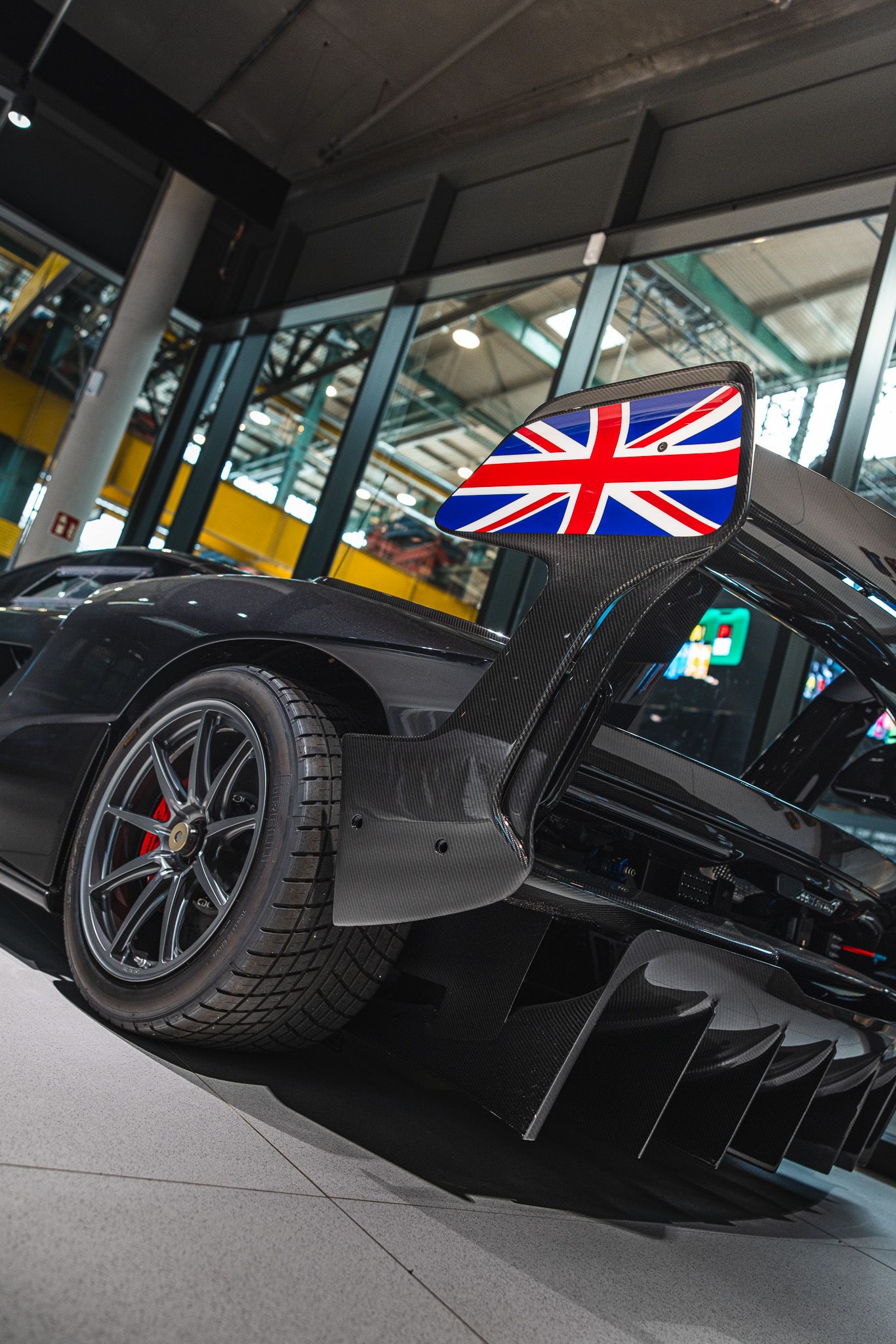 Close-up of a black McLaren supercar rear wheel and diffuser with a Union Jack side mirror detail.