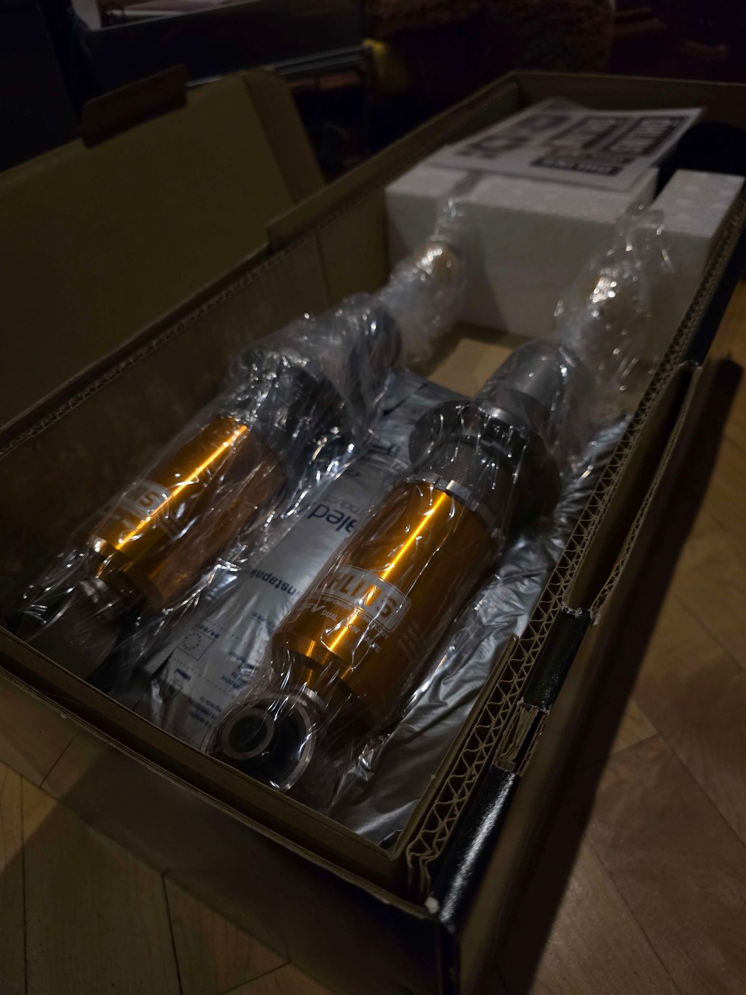 Three yellow coilover shocks packed in protective wrap inside an open cardboard box ready for installation.