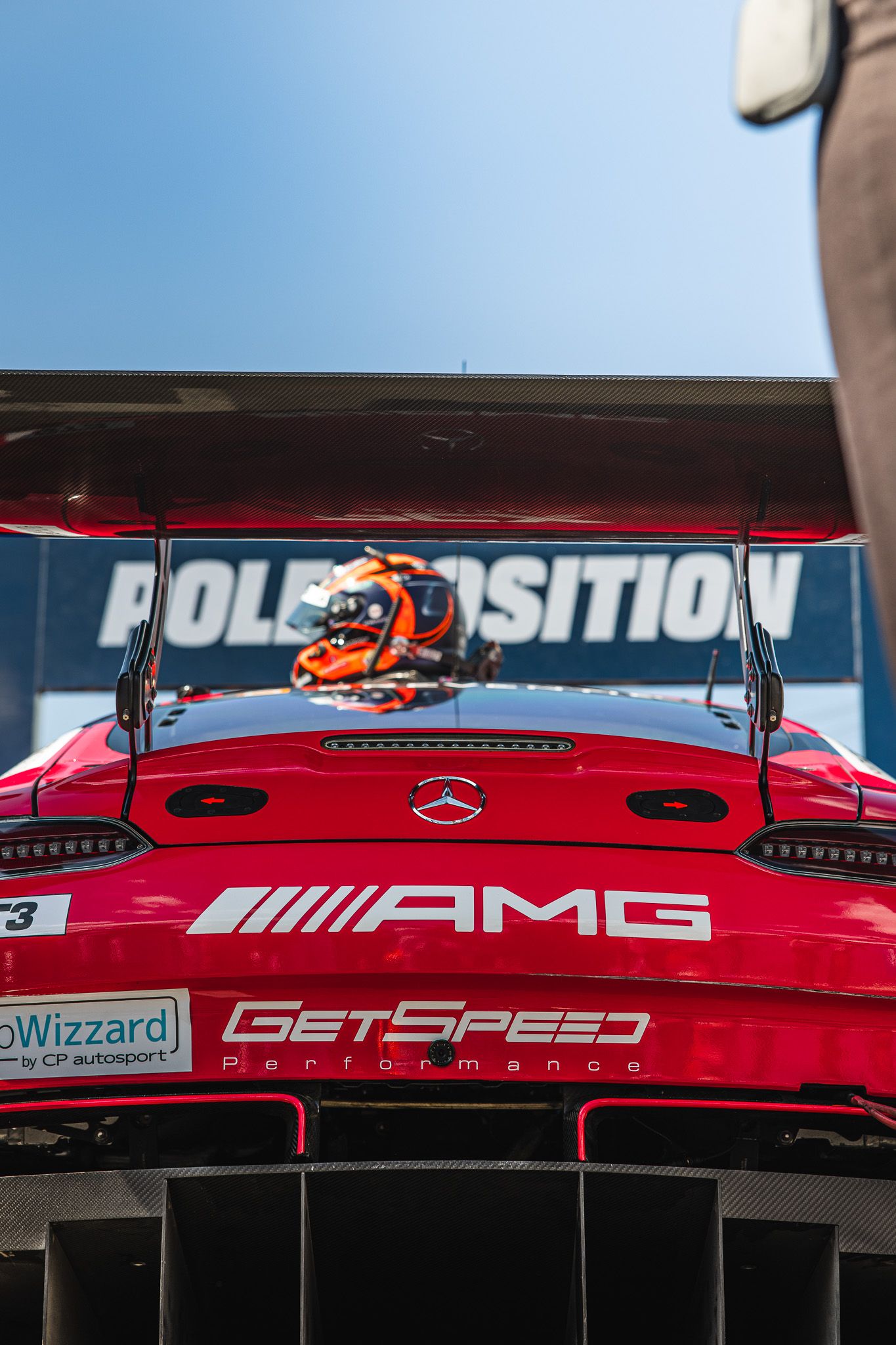 Red Mercedes-AMG GT3 race car from GetSpeed Performance sits at pole position under a clear blue sky.