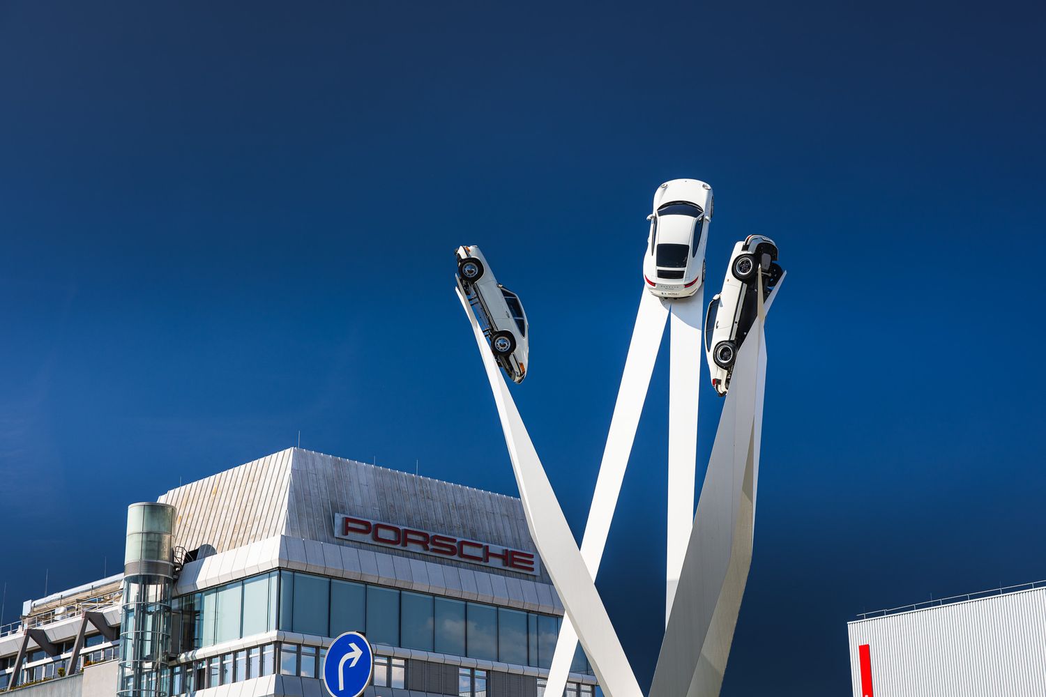 Porsche museum exterior with iconic sculpture of three white Porsche cars mounted on tall pillars.