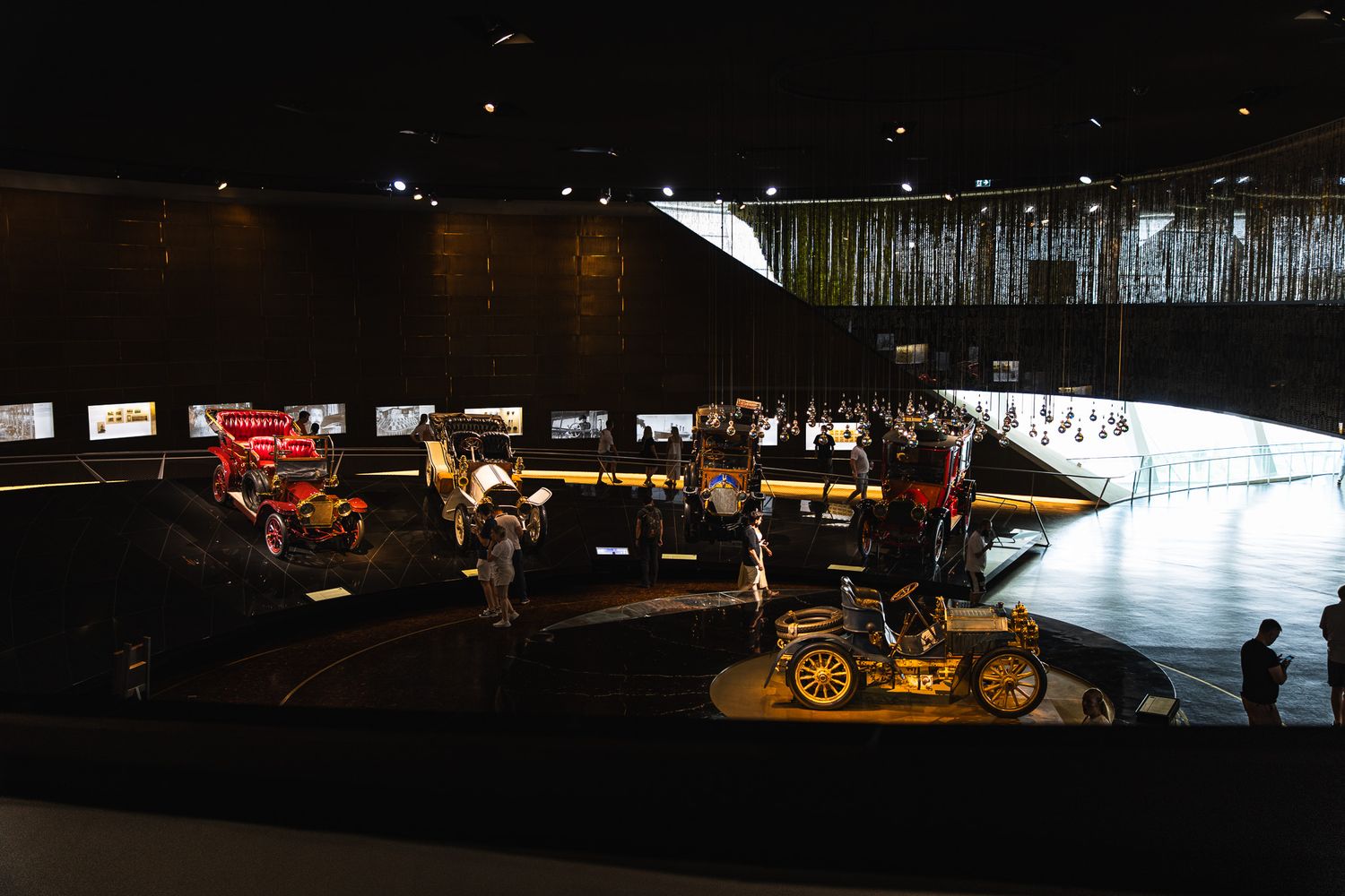 Wide-angle view of a dark automotive museum displaying vintage early 20th century automobiles on a curved floor.