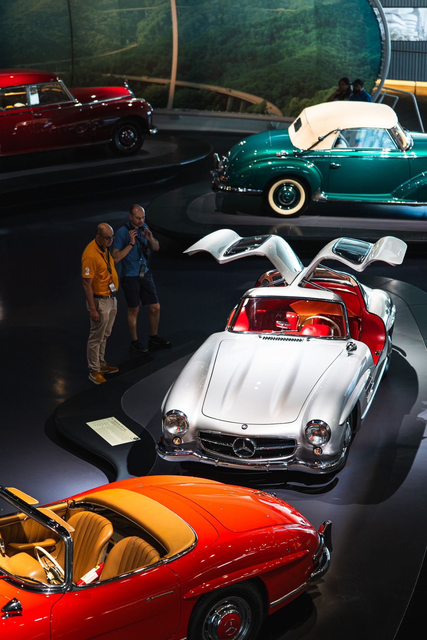 Classic Mercedes-Benz 300SL Gullwing with open doors surrounded by vintage cars in a museum.