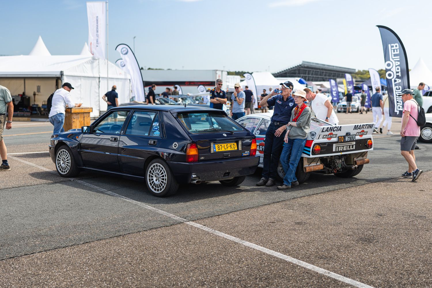 Vintage Lancia rally cars displayed at an outdoor motorsport event with spectators gathered around.