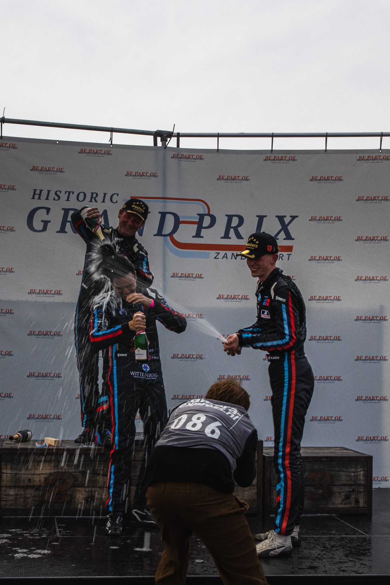 Racing drivers celebrating victory with champagne spray on the Historic Grand Prix Zandvoort podium.
