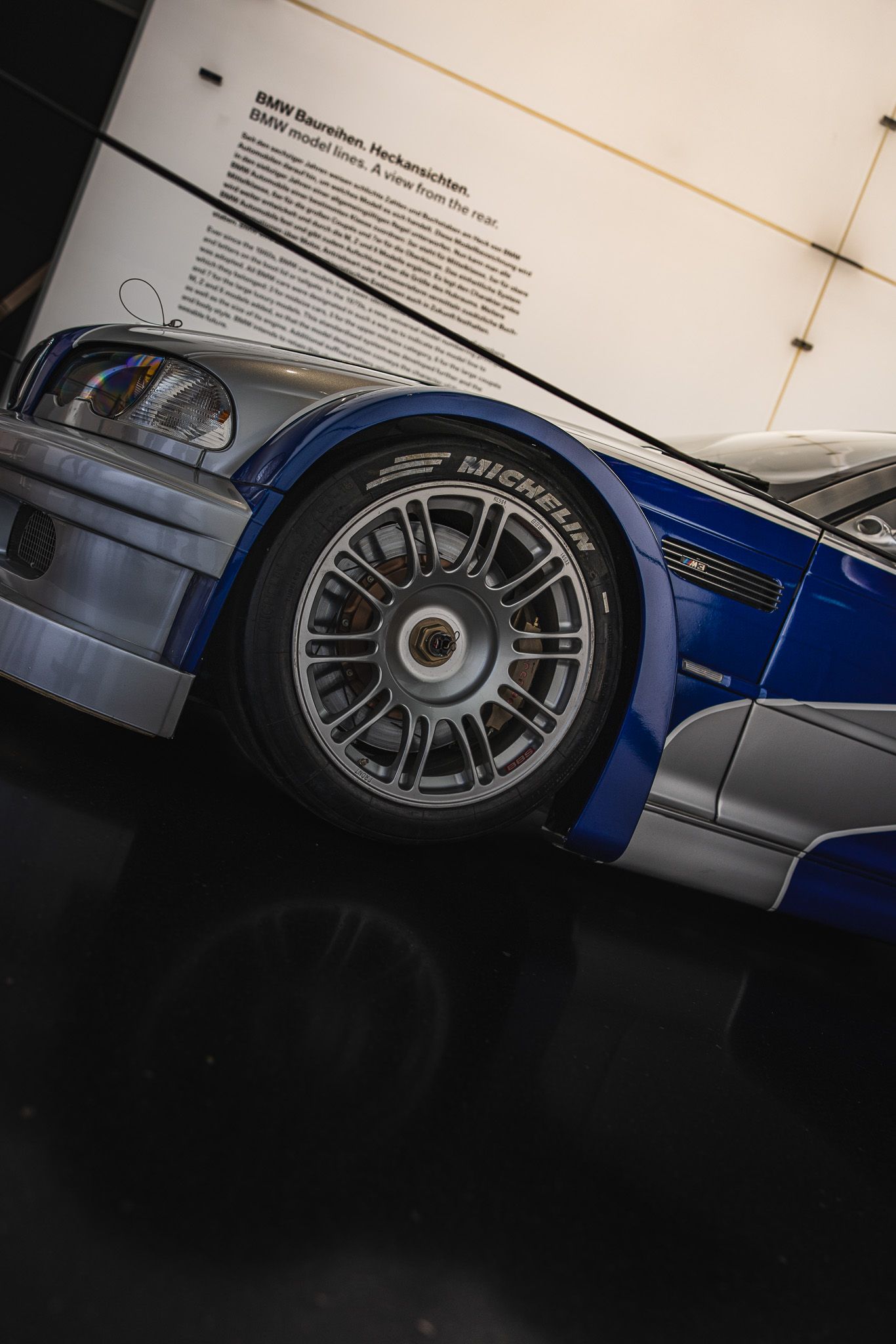 Close-up of a Michelin tire on a blue and silver BMW M3 GTR racing car in a museum.