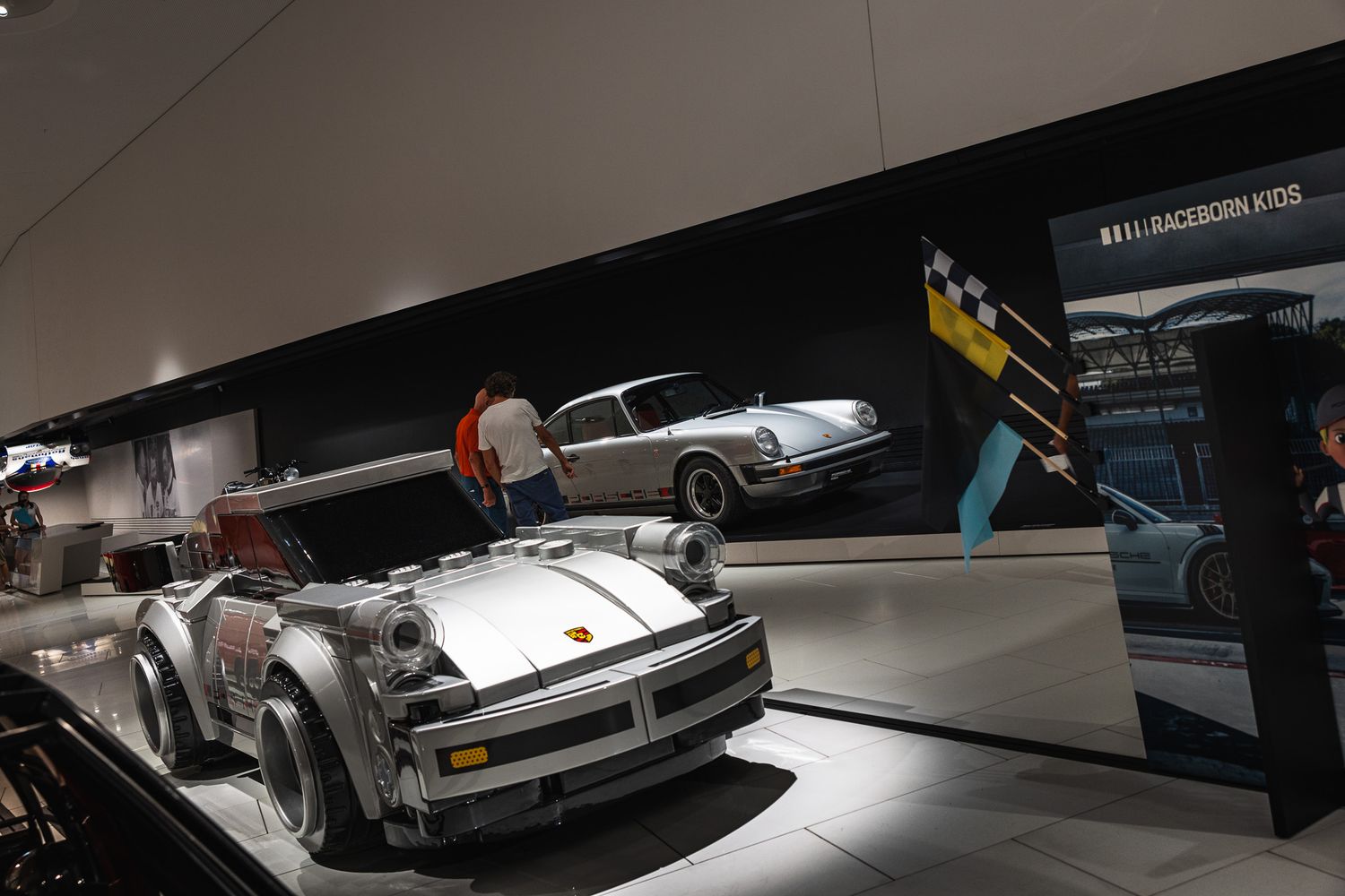 Porsche 911 race car and classic coupe on display in a motorsport museum exhibit with checkered flag backdrop.