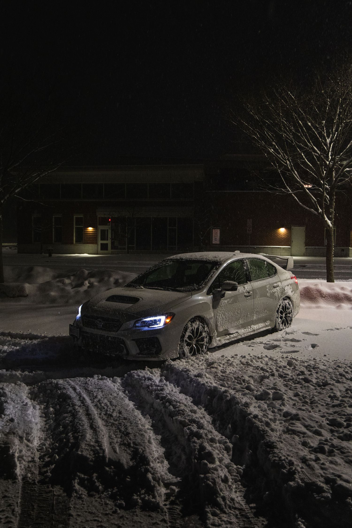 White Subaru WRX STI with blue headlights parked in snowy parking lot at night.