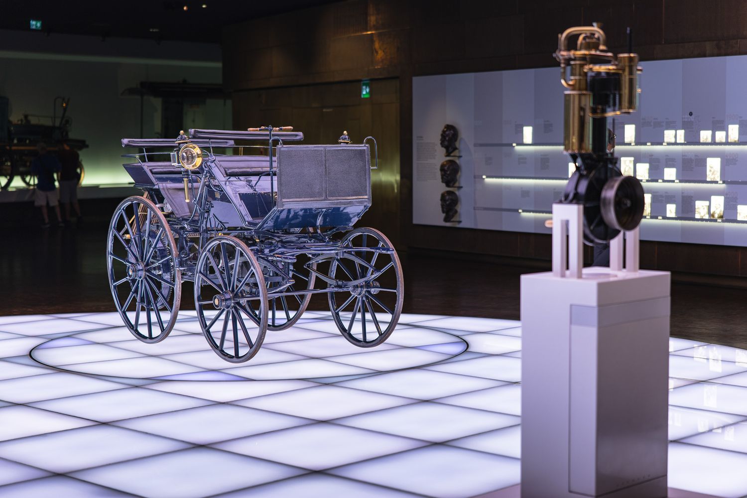 Antique horse-drawn carriage and early engine on display in a brightly lit automotive museum.
