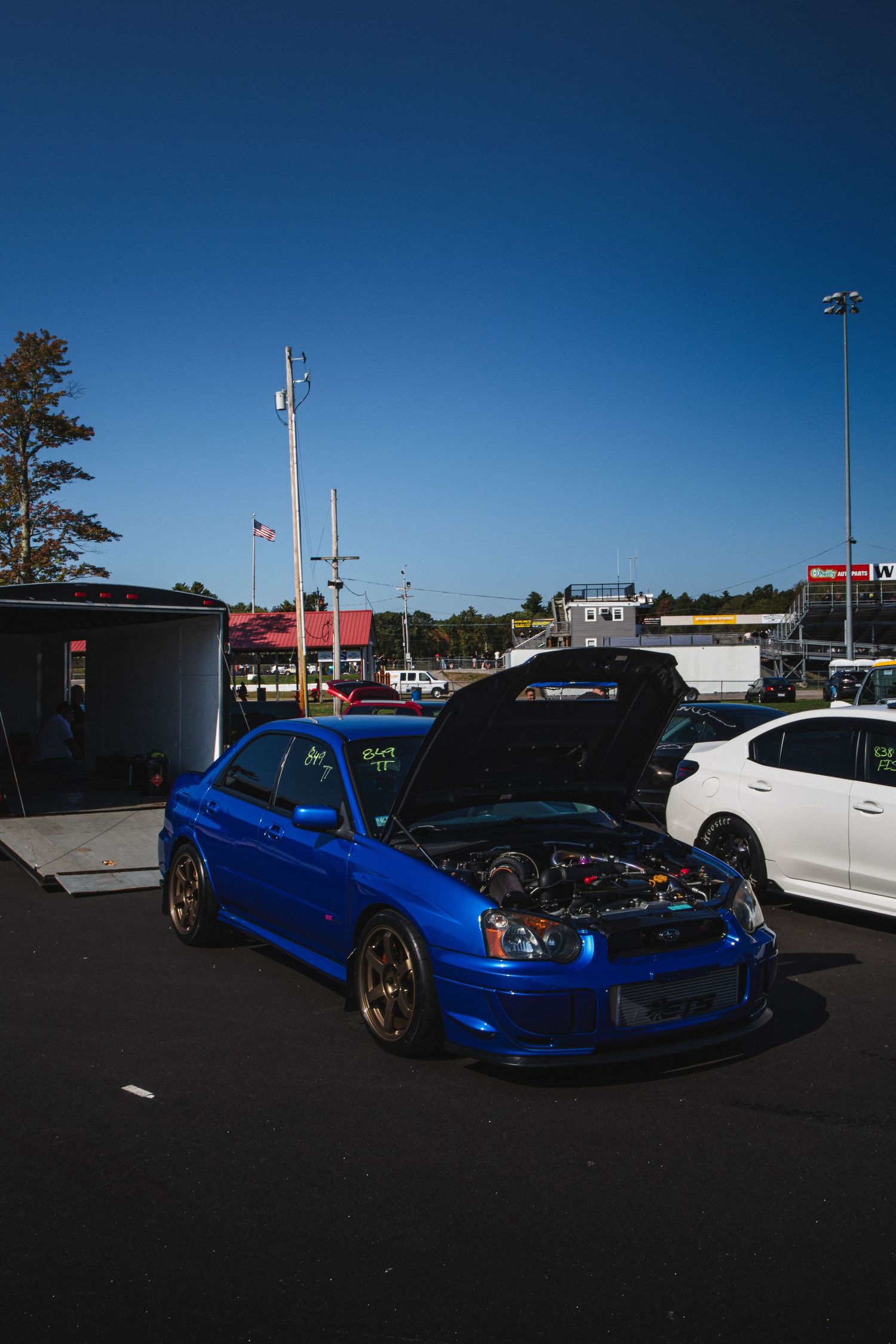 Modified blue Subaru Impreza WRX STI with open hood and gold wheels under clear blue sky.
