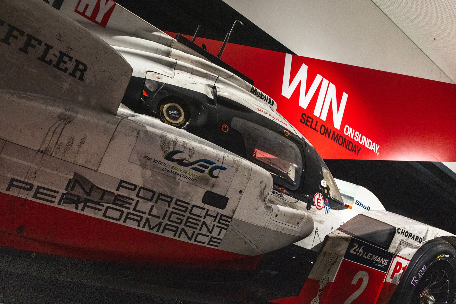 Porsche and Toyota WEC LMP1 race cars on display at an indoor motorsport exhibition.
