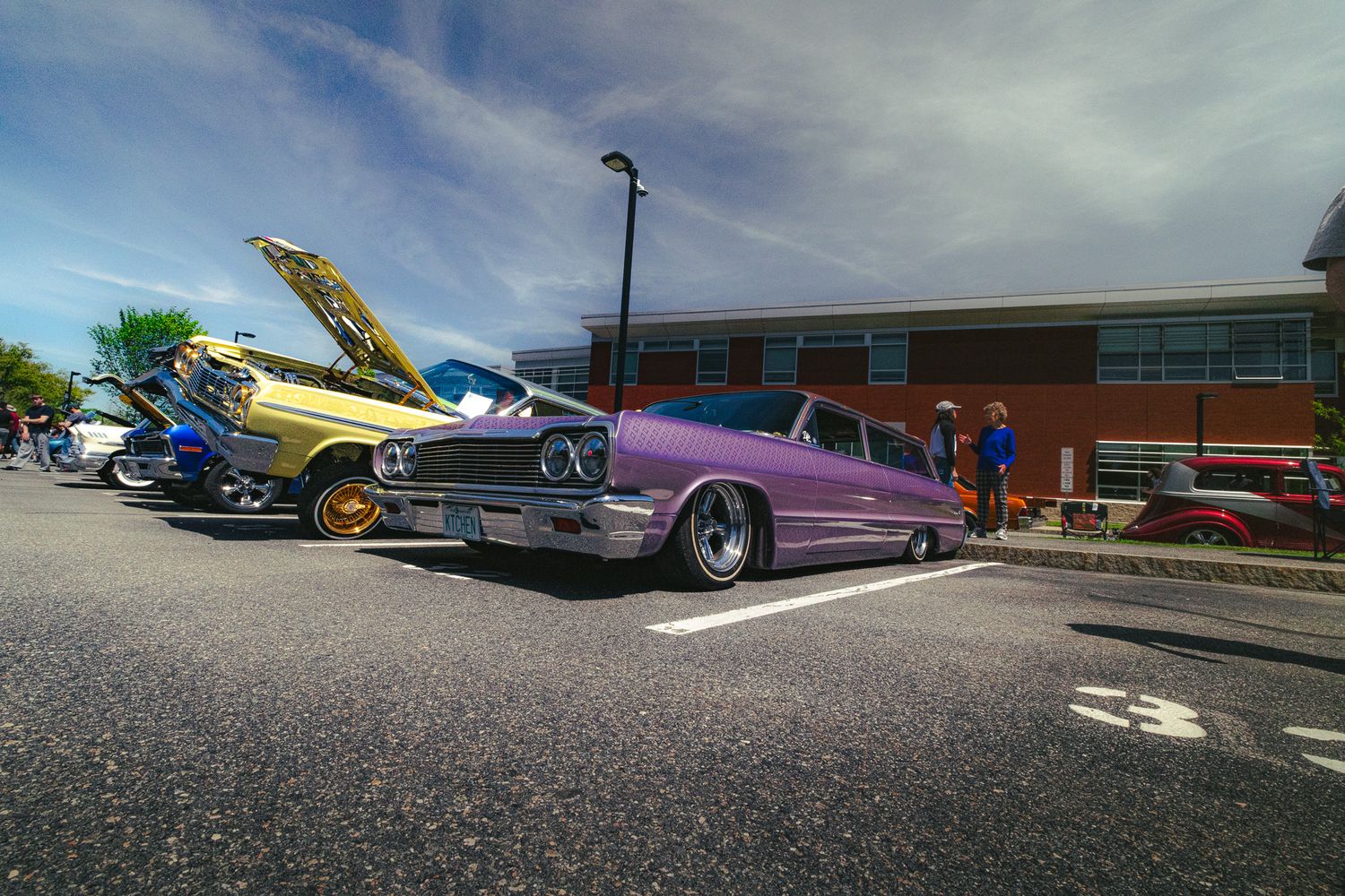 Custom purple 1964 Chevy Impala lowrider with slammed stance at an outdoor car show.