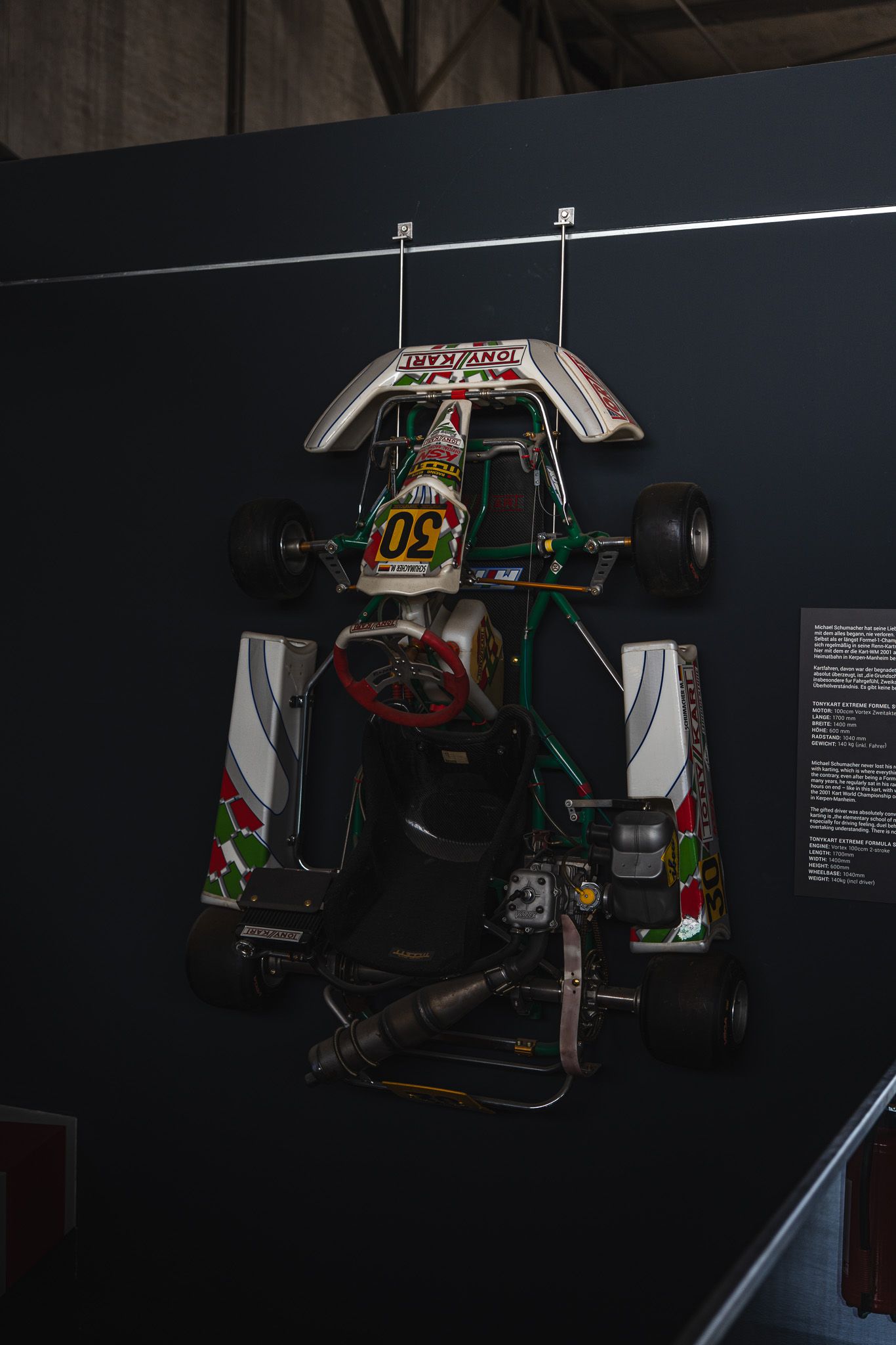 Racing kart number 20 mounted on a dark wall in a motorsport museum exhibit.