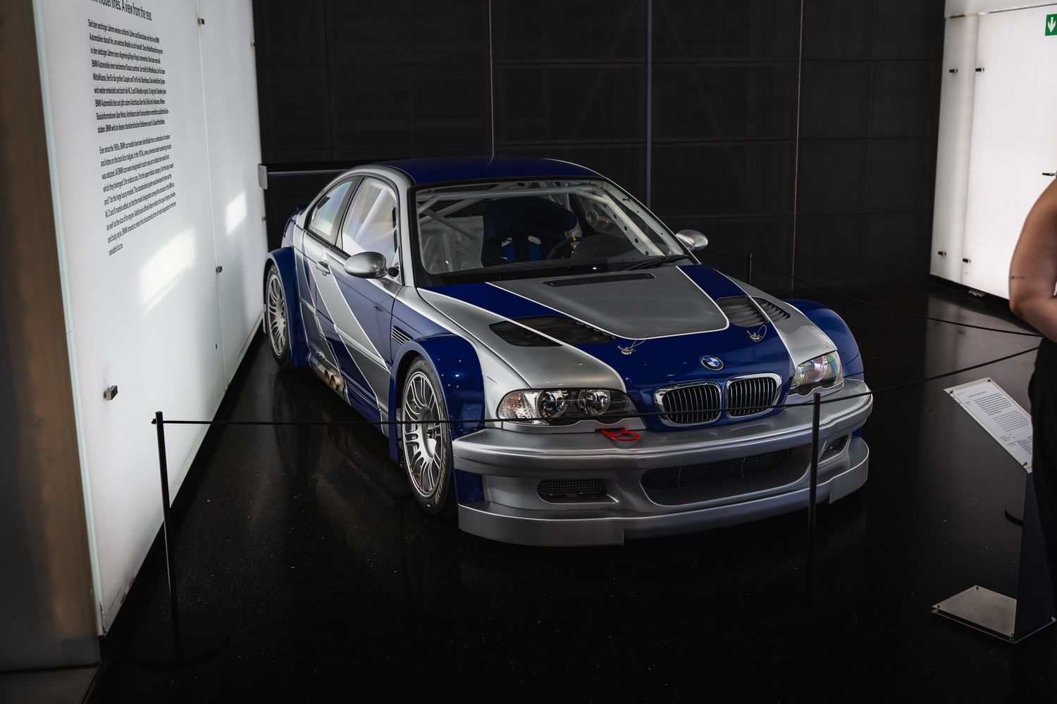 Blue and silver BMW M3 GTR racing car on display in a dimly lit automotive museum exhibit.