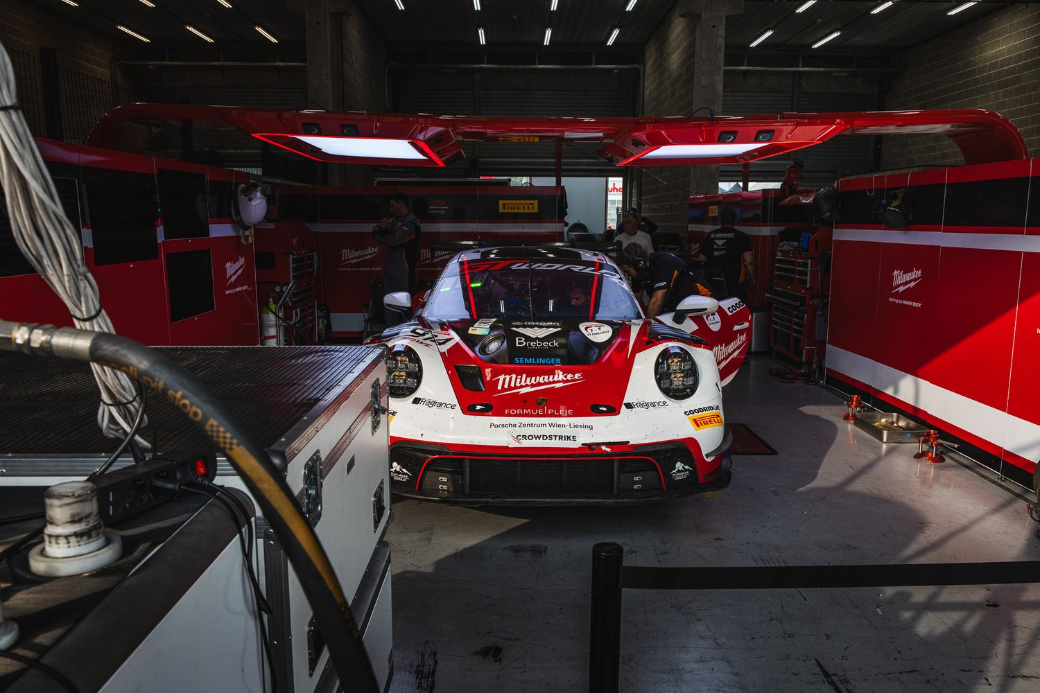 Red and white Milwaukee-sponsored Porsche GT3 race car prepared in team garage at circuit.
