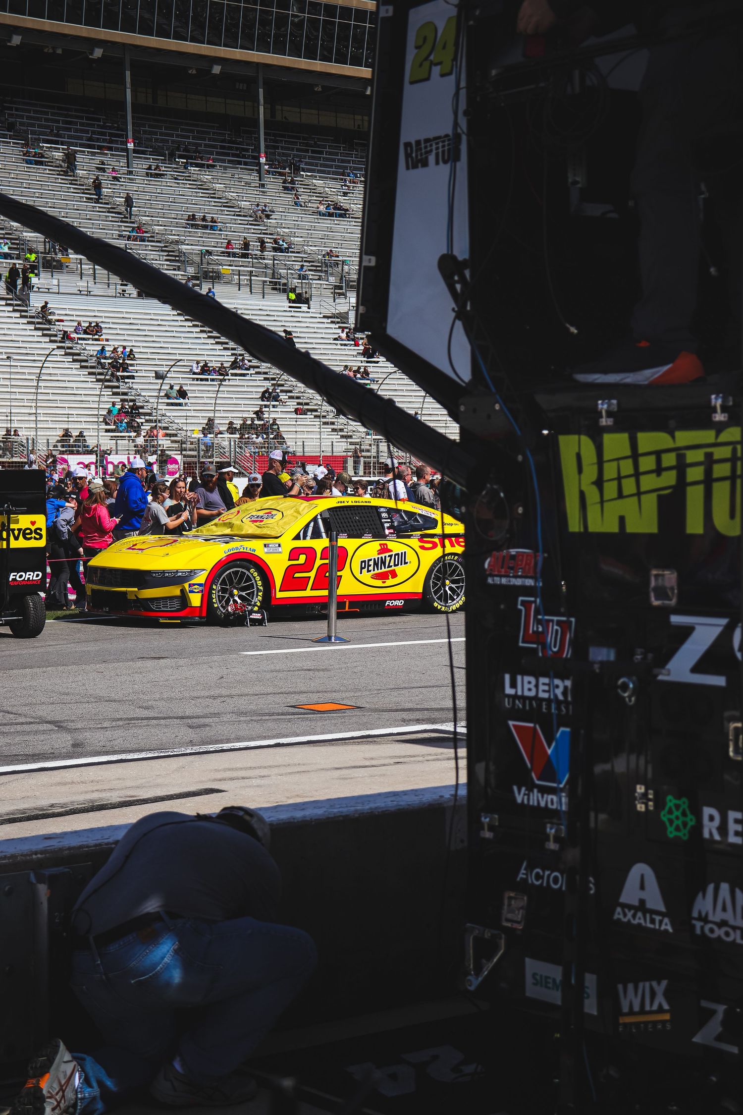 Yellow Shell Pennzoil NASCAR No. 22 Ford Mustang in pit lane at a racing circuit.