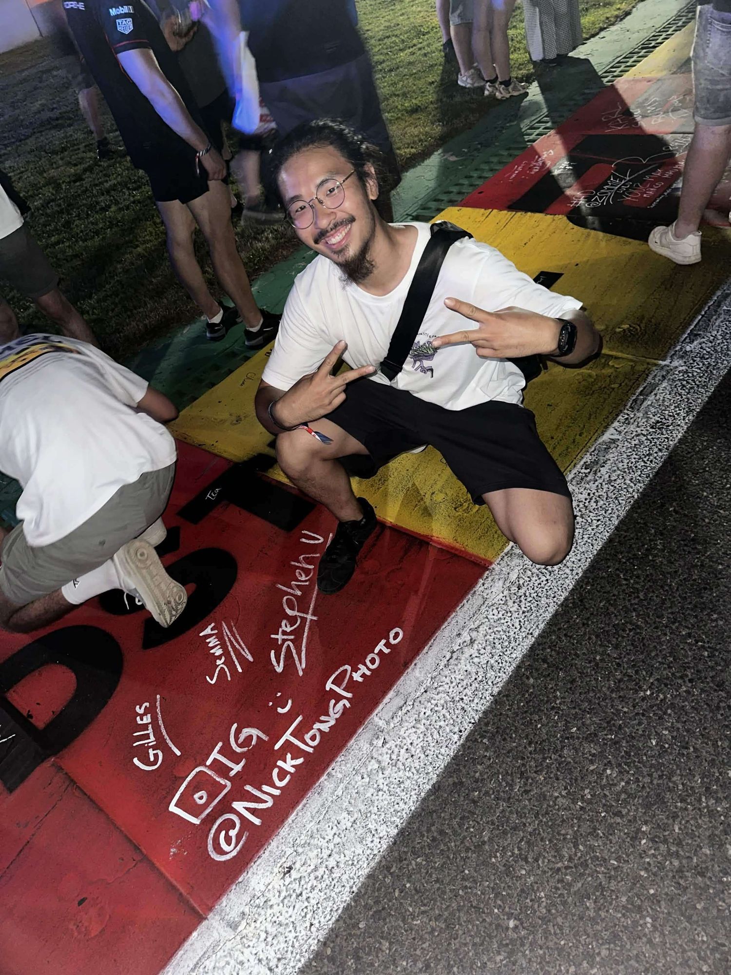 Smiling young man poses on a colorful painted racing circuit surface at a motorsport fan event.