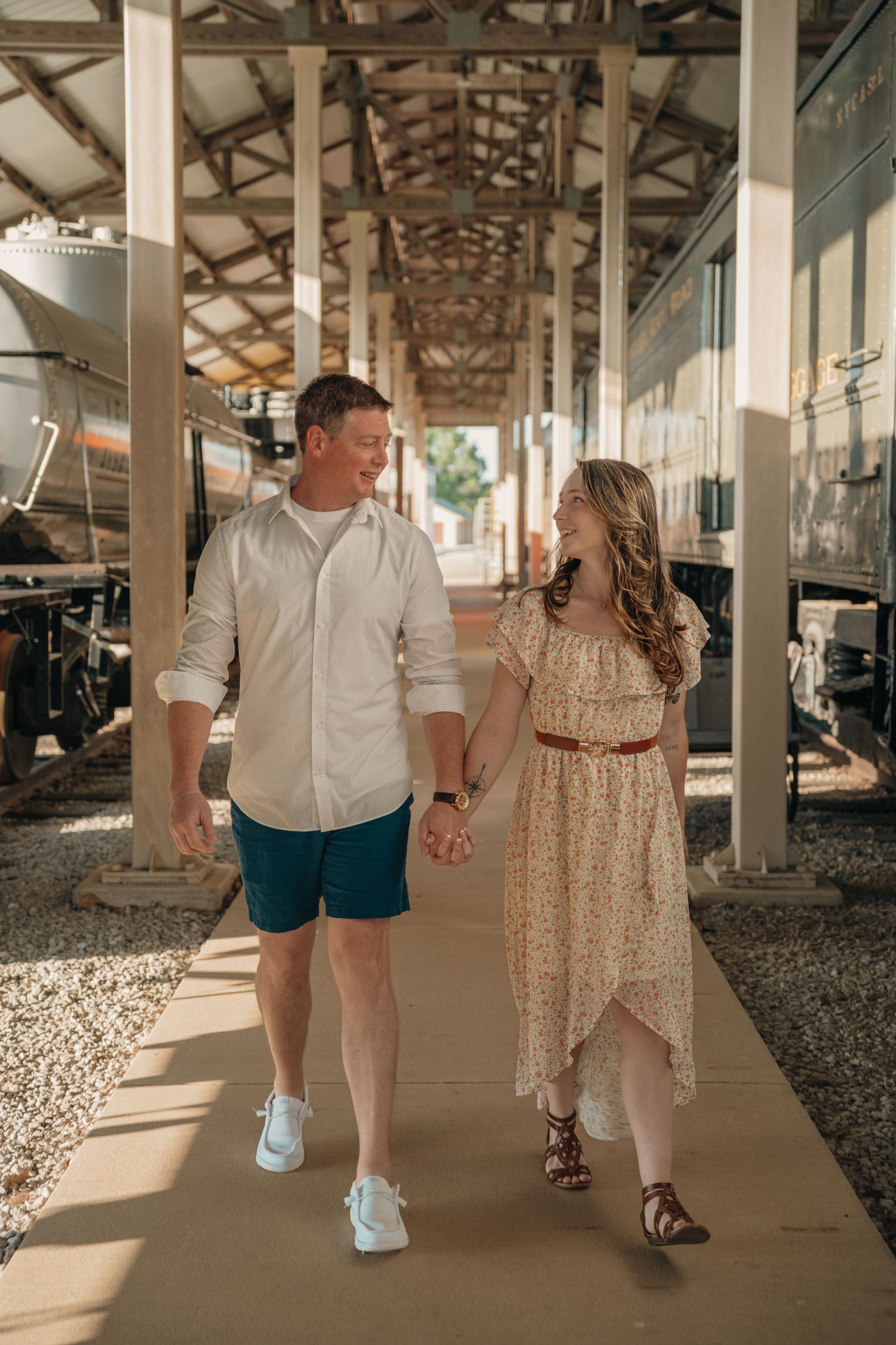 Young couple holding hands and walking together near vintage train cars at a station.