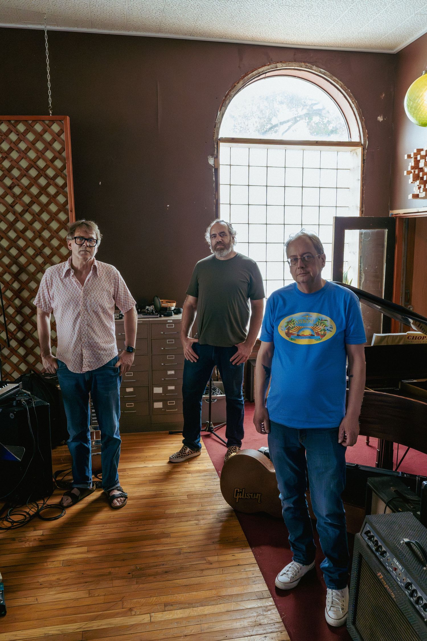 Three male musicians posing in a recording studio with instruments and equipment in a vintage room.