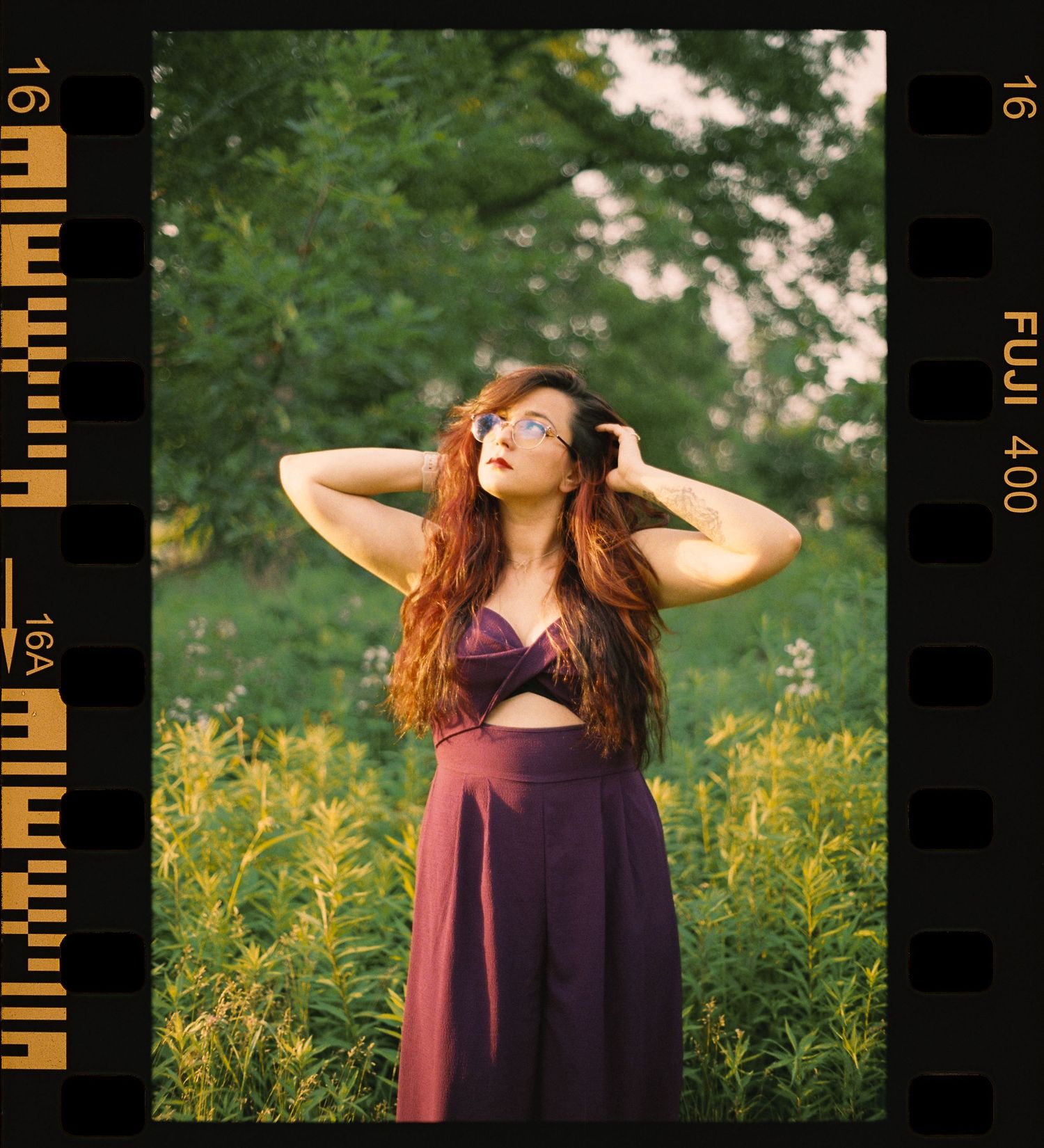 Red-haired woman in purple dress posing in a wildflower meadow on Fuji 400 film format.